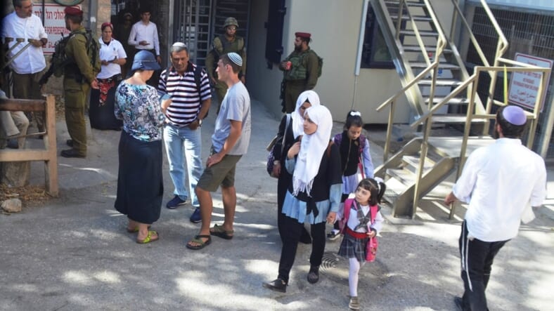 Jewis and Palestinian Arab girls pass at checkpoint in Hebron on Sukkot